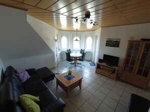 Ein Wohnzimmer mit einem schwarzen Sofa, einem Holztisch, einem Fernsehschrank und einem Essbereich mit Tisch und Stühlen.