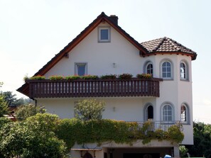 Ein zweigeschossiges Haus mit Balkon, kleinem Fenster und einem Ziegeldach.
