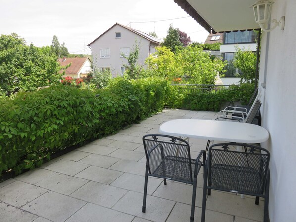 A patio with a white table and two chairs, surrounded by greenery and houses in the background. - Vacation apartment type 3, 38sqm, 1 bedroom, max. 2 persons, 1 - 2 persons - (Vogtsburg im Kaiserstuhl)