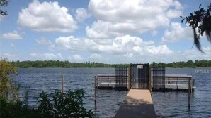 A wooden dock leading to a gated entrance over water, surrounded by greenery.