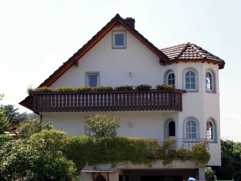 A two-story house with a balcony, a small window, and a tiled roof.