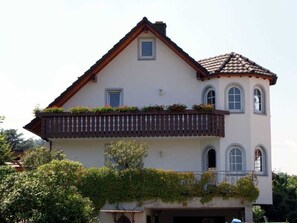 A two-story house with a balcony, a small window, and a tiled roof.