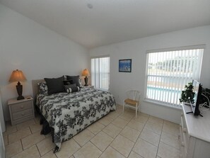 A bedroom with a bed, two bedside tables with lamps, a chair, a desk with a computer, and a window with blinds.