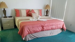 Una camera da letto con un letto, due comodini, lampade, un tappeto verde e una finestra con persiane.