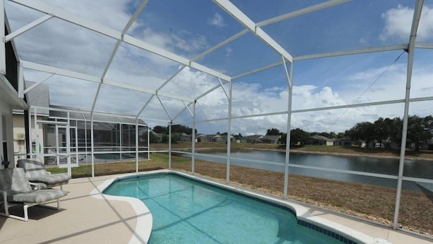 Una piscina con un patio coperto, vista su un corpo d'acqua e cielo sereno.