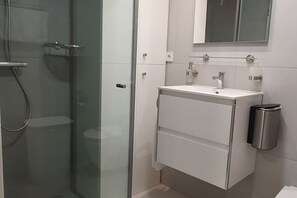 A modern bathroom with a glass-enclosed shower, a white vanity with a mirror, and a trash can. - ecoSmart Apartments Living (Granada)