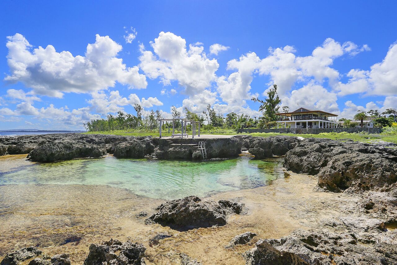 A coastal area with clear water, rocky terrain, and a large building with a balcony overlooking the water.