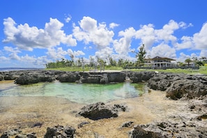 A coastal area with clear water, rocky terrain, and a large building with a balcony overlooking the water.