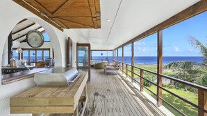 Un balcon spacieux doté d’un plancher en bois, d’un coin salon avec des coussins et d’une vue sur l’océan.
