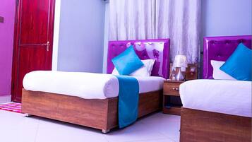 A hotel room with two beds, a wooden wardrobe, a nightstand with a lamp, and a window with curtains.
