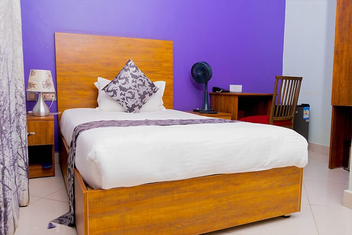 A neatly made bed with a wooden headboard, a bedside table with a lamp, and a small fan.