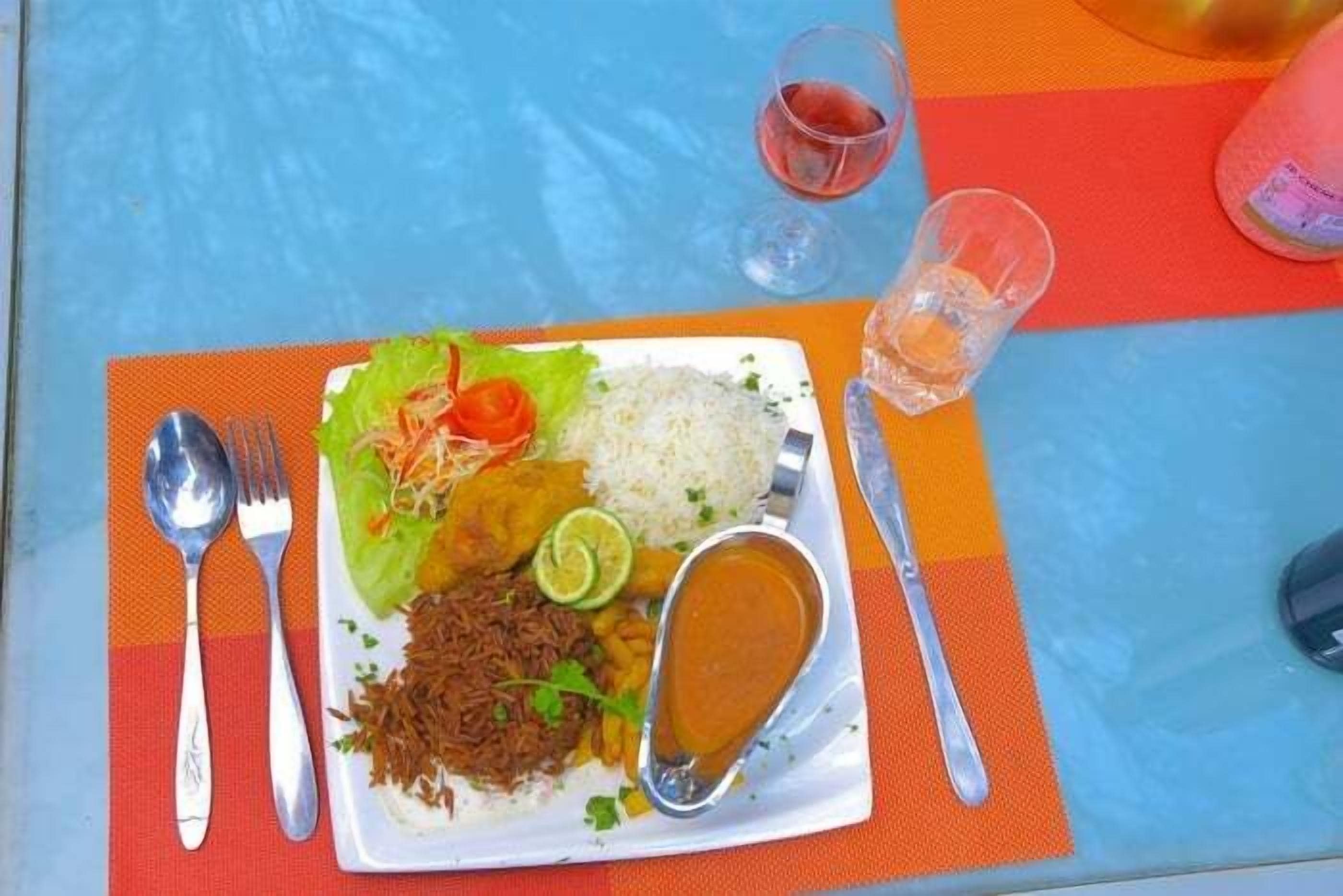 Plato con arroz, verduras y salsa, acompañado de cubiertos y un vaso de bebida roja sobre una mesa.