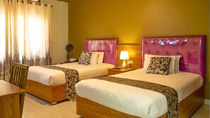 Une chambre d’hôtel avec deux lits, une chaise en bois, une table de chevet avec une lampe et une fenêtre avec des rideaux.