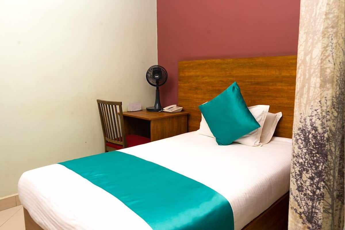 A neatly made bed with a teal bedspread, a wooden headboard, and a single teal pillow.