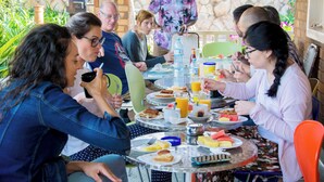 Un groupe de personnes est assis à une table en plein air et prend son petit-déjeuner, avec divers plats à disposition.