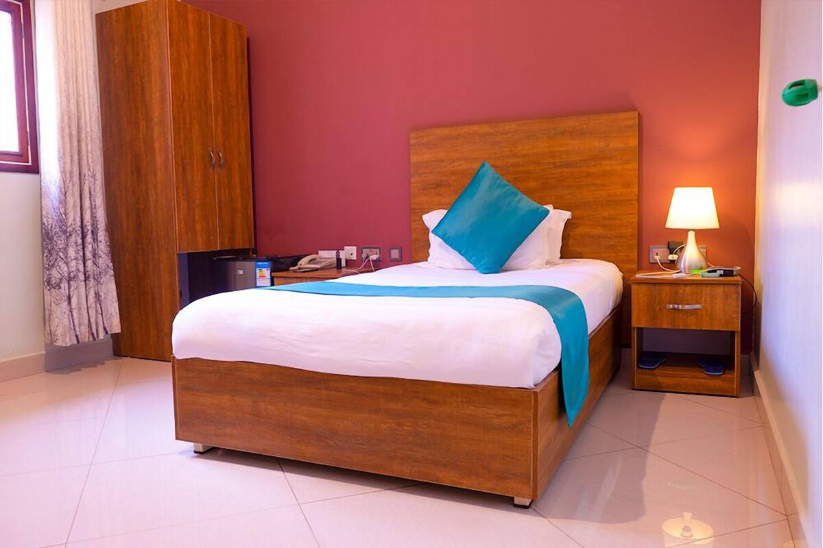 A neatly made bed with a wooden headboard, a nightstand with a lamp, and a wardrobe in a hotel room.