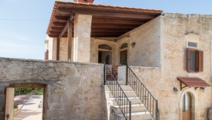 A stone building with a staircase leading to an upper level, featuring a wooden door and a window with shutters. - Afroditi's House  Relax in Crete (Mylopotamos)