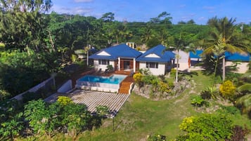 Situated in a lush landscape, this two-story house offers a pool and deck area surrounded by tropical plants and palm trees.