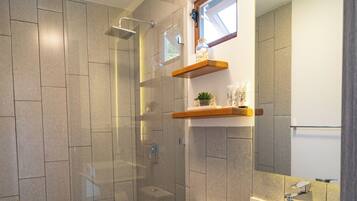 Un baño moderno con ducha de vidrio, inodoro blanco y lavamanos con espejo.