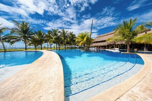 A large, curved swimming pool with clear blue water, surrounded by palm trees and a thatched-roof structure. - Villas La Mar (Taxisco)