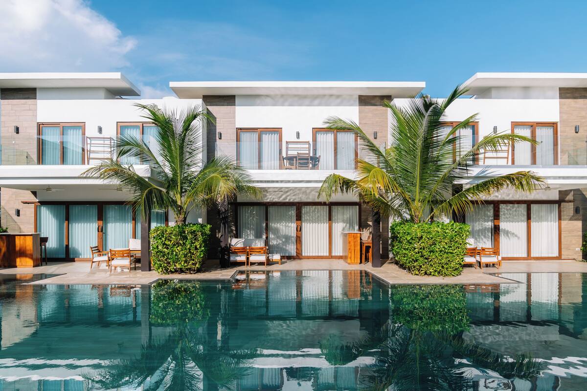 Un hotel moderno con piscina, zona de estar exterior y palmeras.