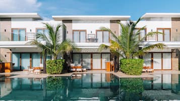 A modern hotel with a swimming pool, outdoor seating, and palm trees.