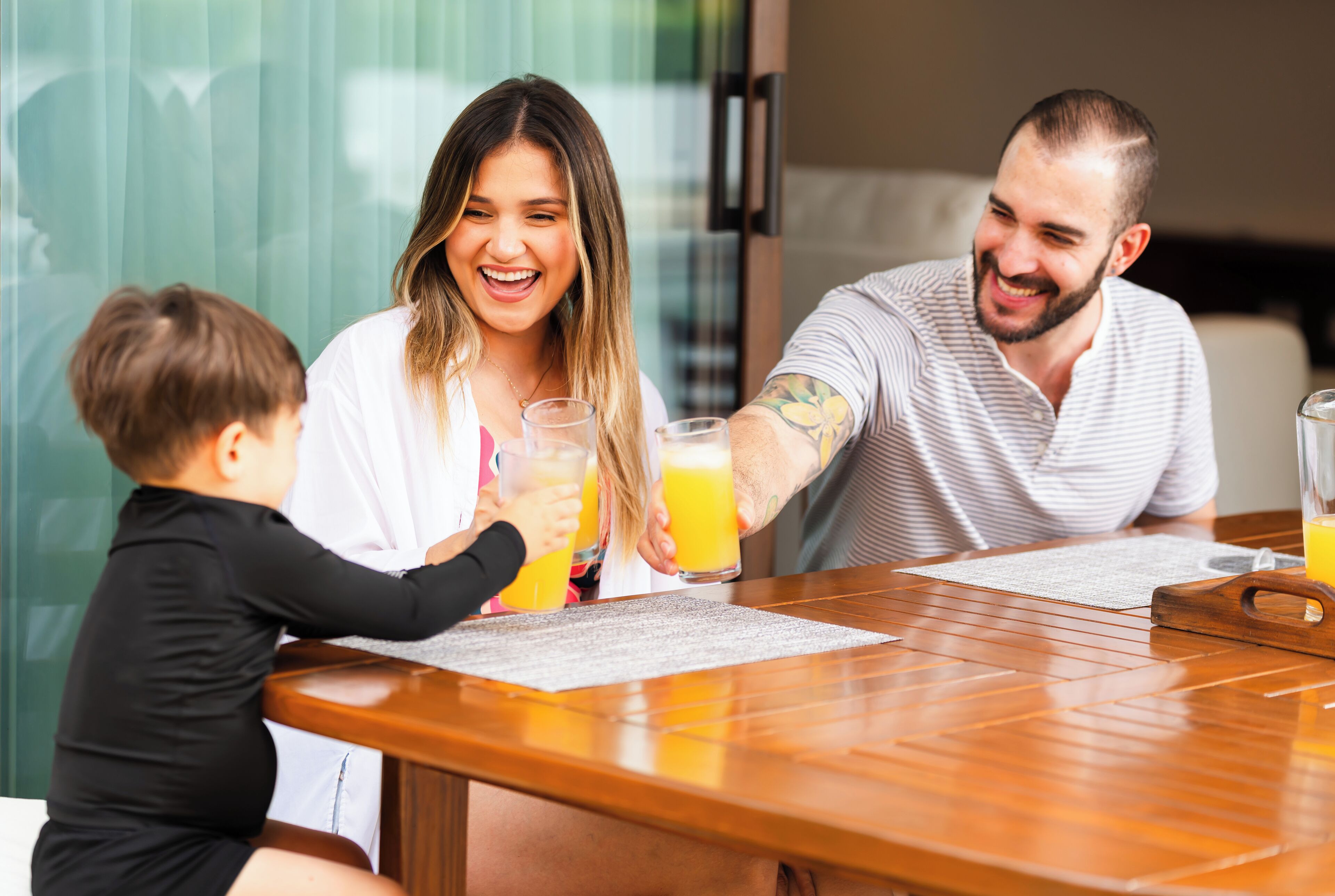 Une famille de trois personnes est assise autour d’une table en bois, devant un menu, avec des verres de jus d’orange et une bouteille d’eau.