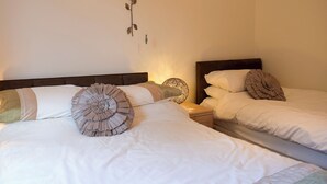 Two beds with white bedding and decorative pillows, a wall-mounted flower decoration, and a textured wall hanging.