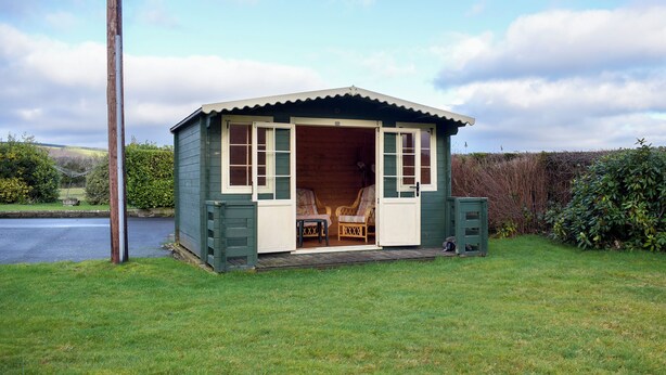 A small, single-story wooden cottage with a porch, a chair, and a table.
