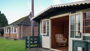 A wooden house with a porch, a chair inside, and a grassy yard.