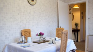 A dining area with a table set for two, a clock on the wall, and a door leading to another room.