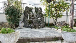 Un chemin de pierre mène à une formation rocheuse ornée de statues, le tout étant entouré de plantes en pot et d’une clôture.