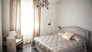 Une chambre à coucher comprenant un lit, une chaise, une table de chevet, une lampe et un lustre.