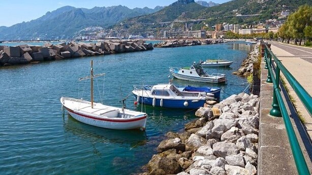Un port où des bateaux sont amarrés, une digue en pierre et une montagne en arrière-plan.