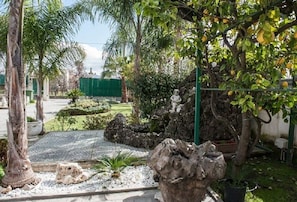 A landscaped garden with a rock formation, palm trees, and a statue.