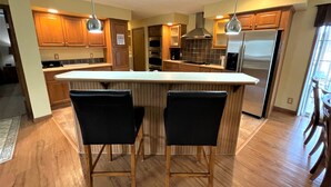 A modern kitchen with wooden cabinets, a central island with bar stools, stainless steel appliances, and pendant lighting. - Copal on Lake Shore @ Spring Brook Resort (Wisconsin Dells)