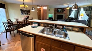 A compact kitchen with a dishwasher, double sink, and a sign instructing not to remove kitchen items from home. - Copal on Lake Shore @ Spring Brook Resort (Wisconsin Dells)