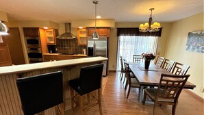 A modern kitchen with a central island, wooden dining table, and chairs. - Copal on Lake Shore @ Spring Brook Resort (Wisconsin Dells)
