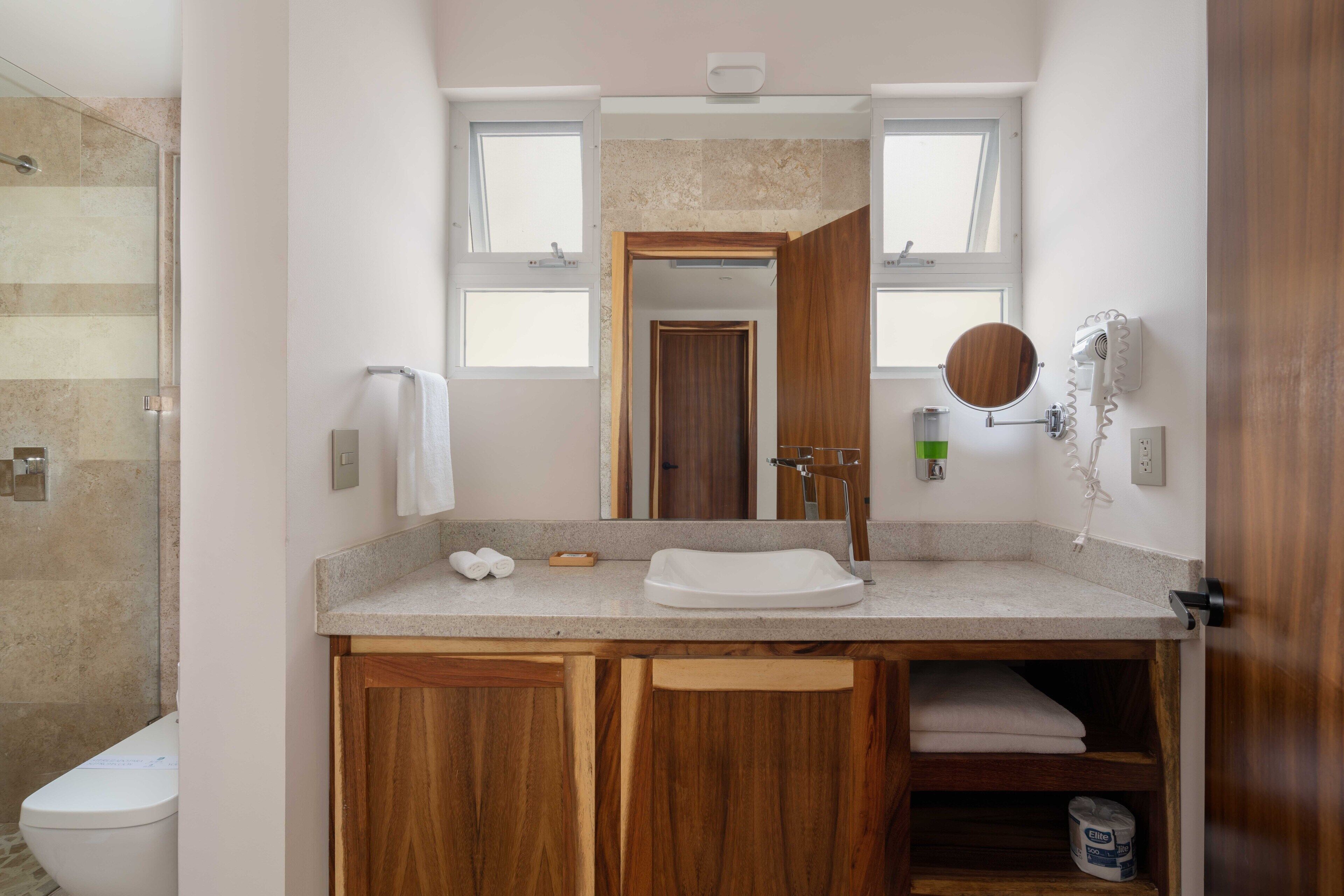 Un baño con tocador de madera, lavabo, espejo y zona de ducha.