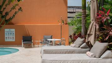 A poolside area with a lounge chair, a small table, and a chair. There is a sign on the wall and a plant to the left.