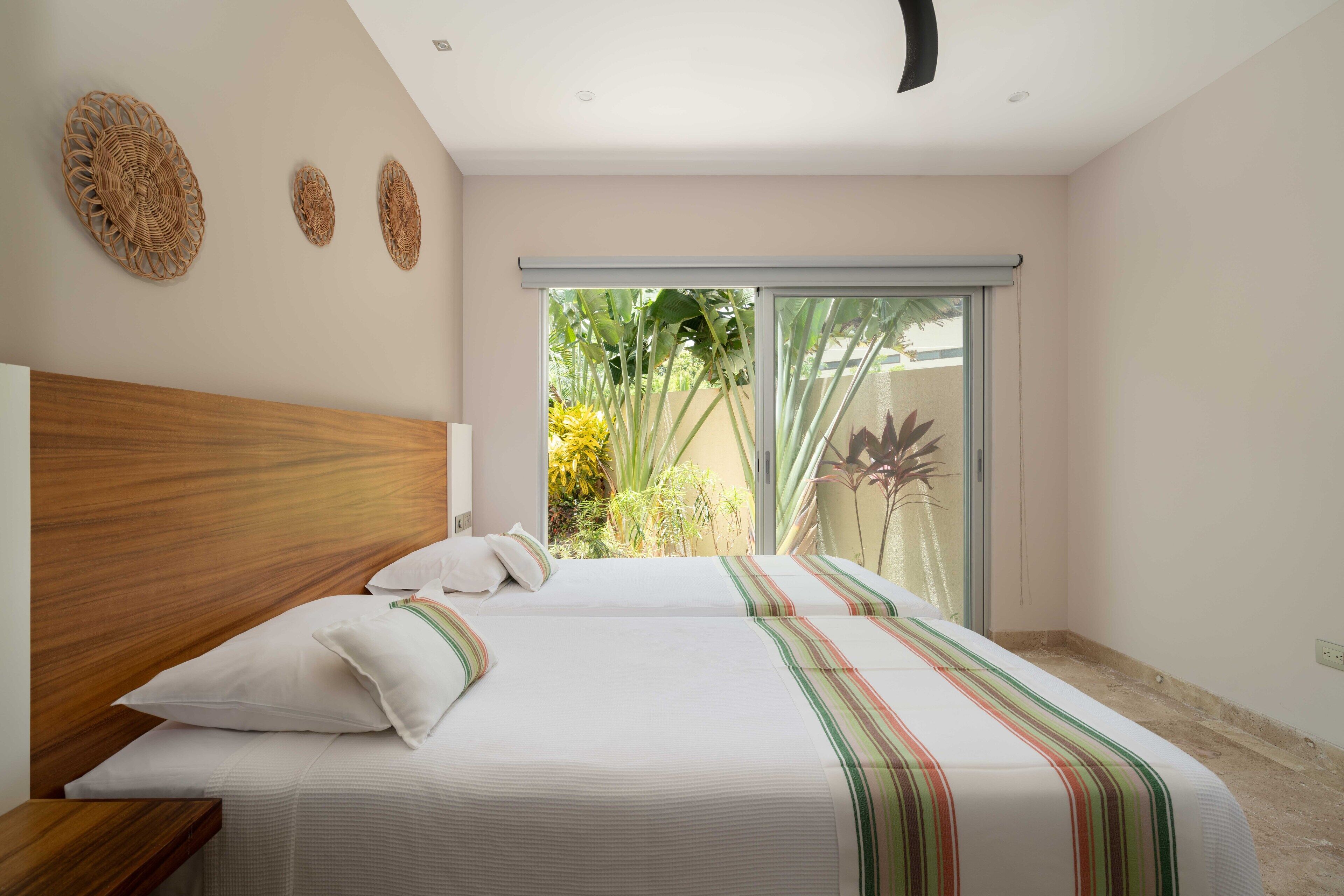 A bedroom with a large bed, wooden headboard, and a view of greenery through a sliding door.