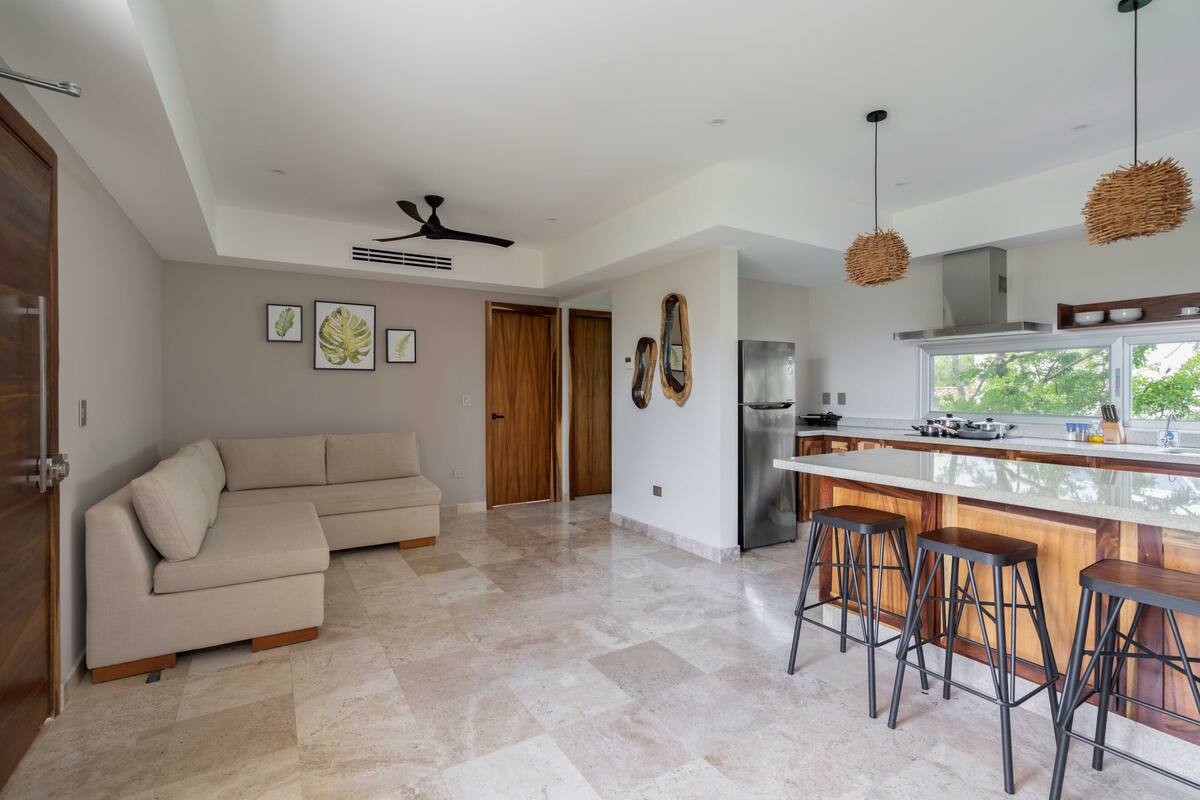 A modern kitchen with a central island, bar stools, and a ceiling fan.