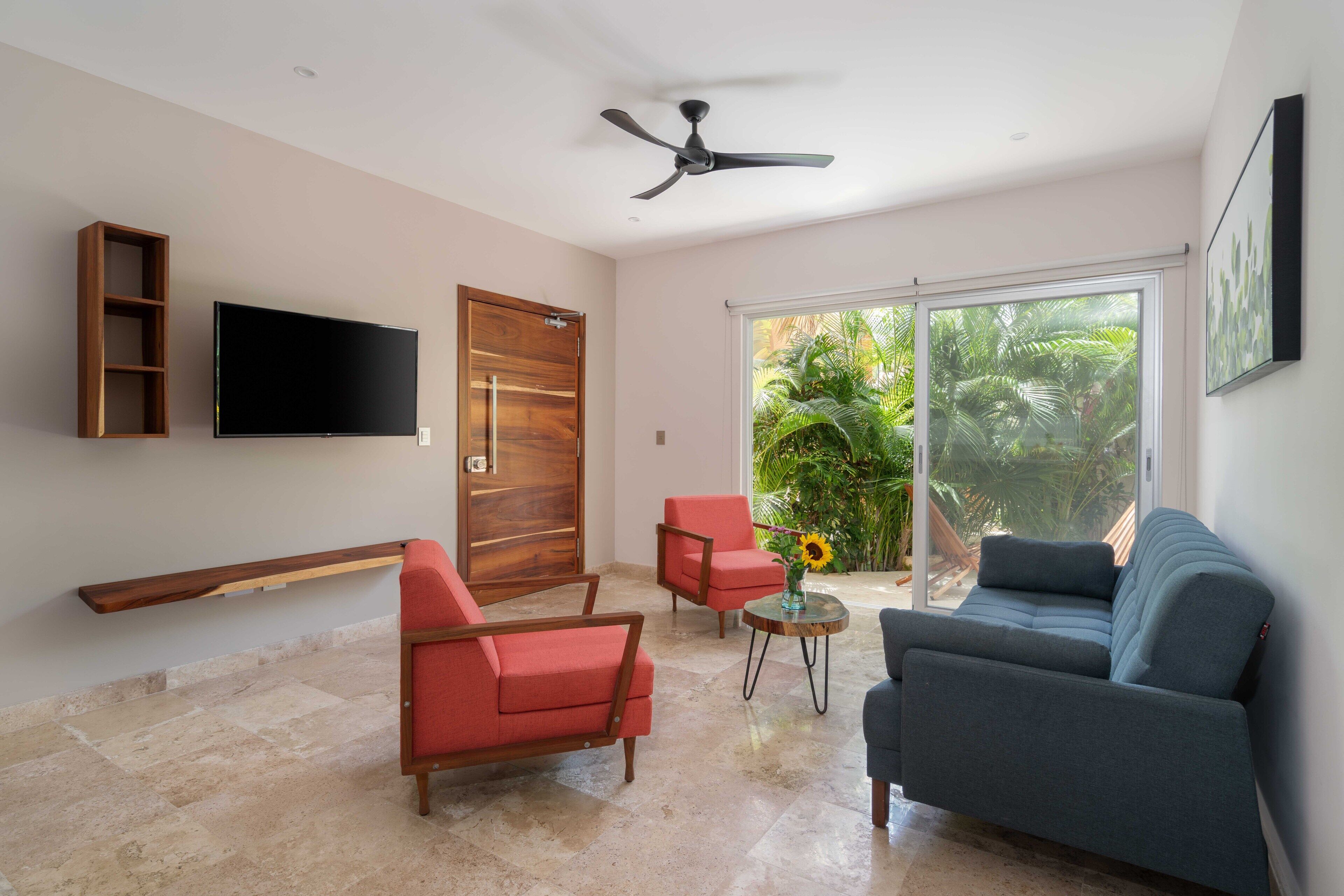 A modern living room with a flat-screen TV, two sofas, a wooden shelf, and a ceiling fan.