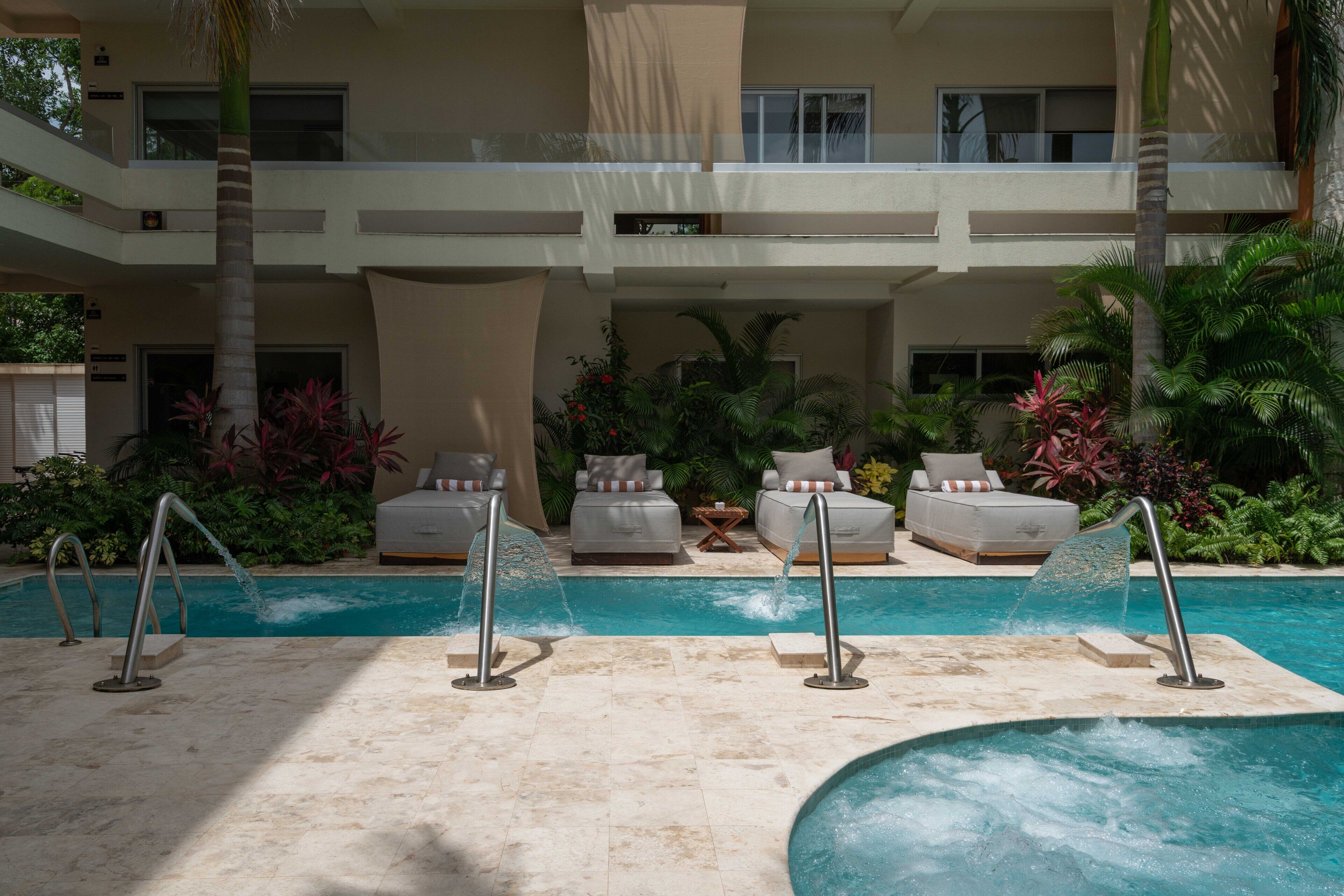 A pool area with two lounge chairs, a water feature, and a view of a multi-story building.