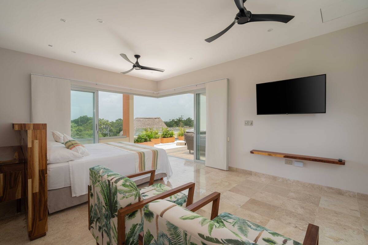 A modern bedroom with a bed, a TV, and a balcony with a view.