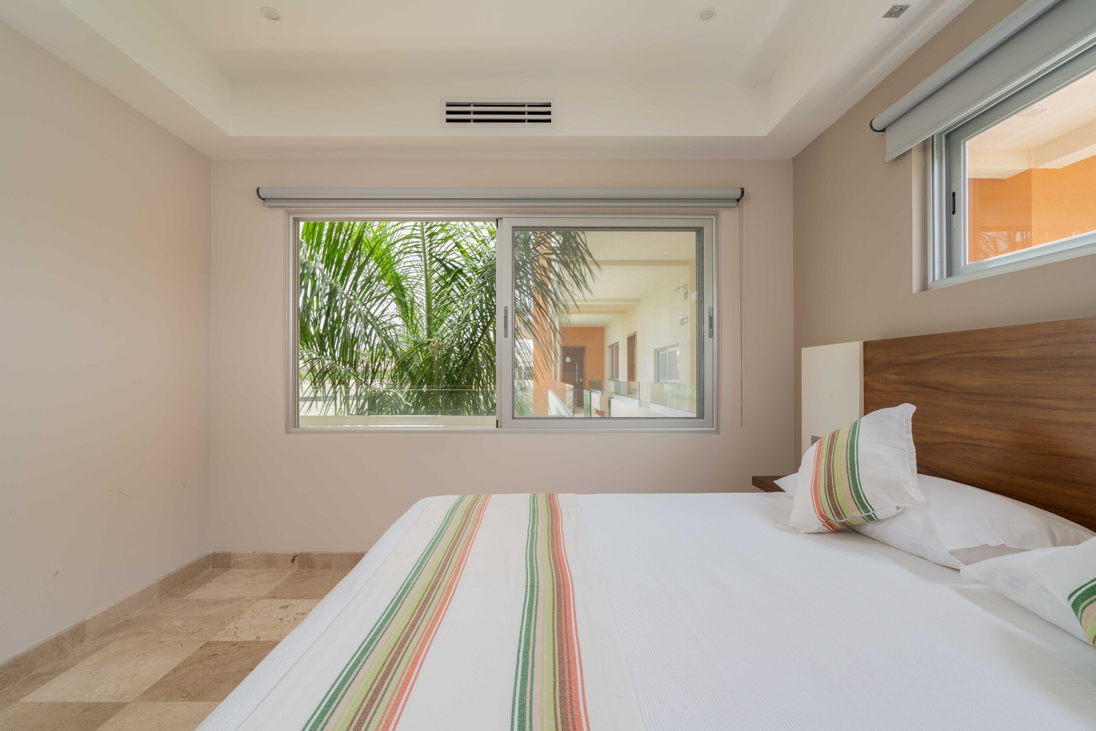 A bedroom with a large bed, a window with a view of palm trees, and a wooden headboard.