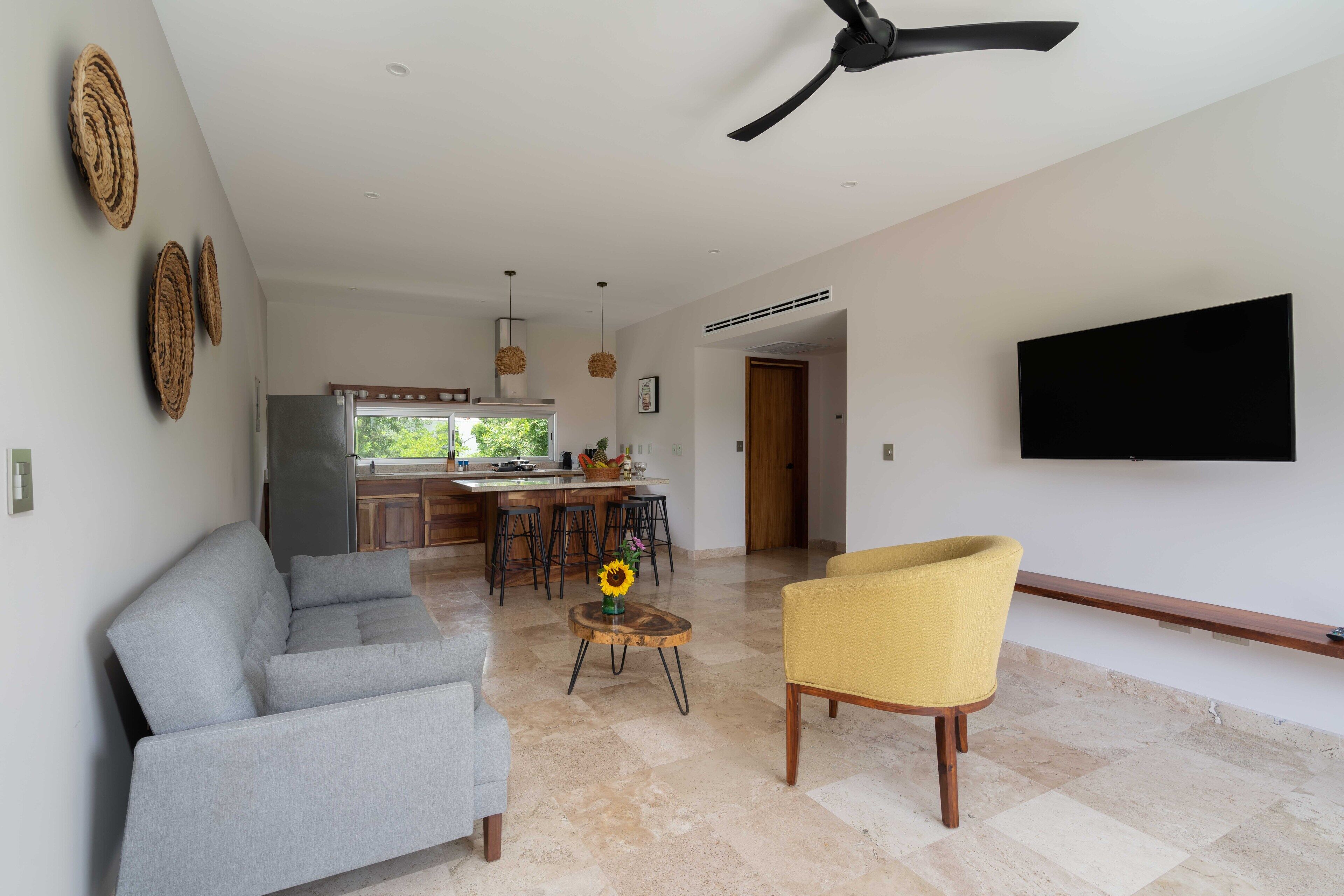 A modern living room with a grey sofa, a yellow armchair, and a TV mounted on the wall.