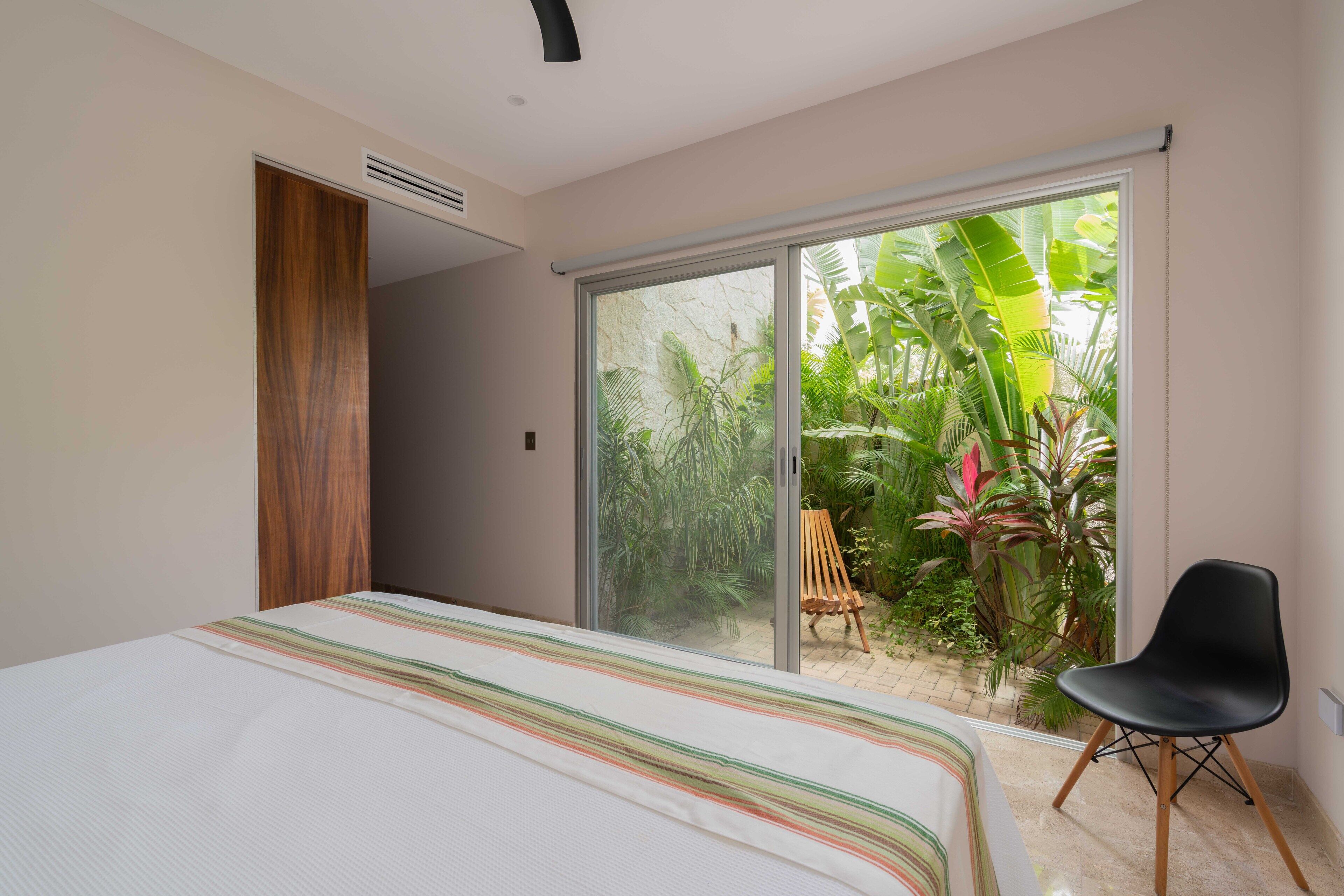 Une chambre à coucher comprenant un lit, une porte-fenêtre coulissante donnant sur un balcon, une chaise et une armoire en bois.
