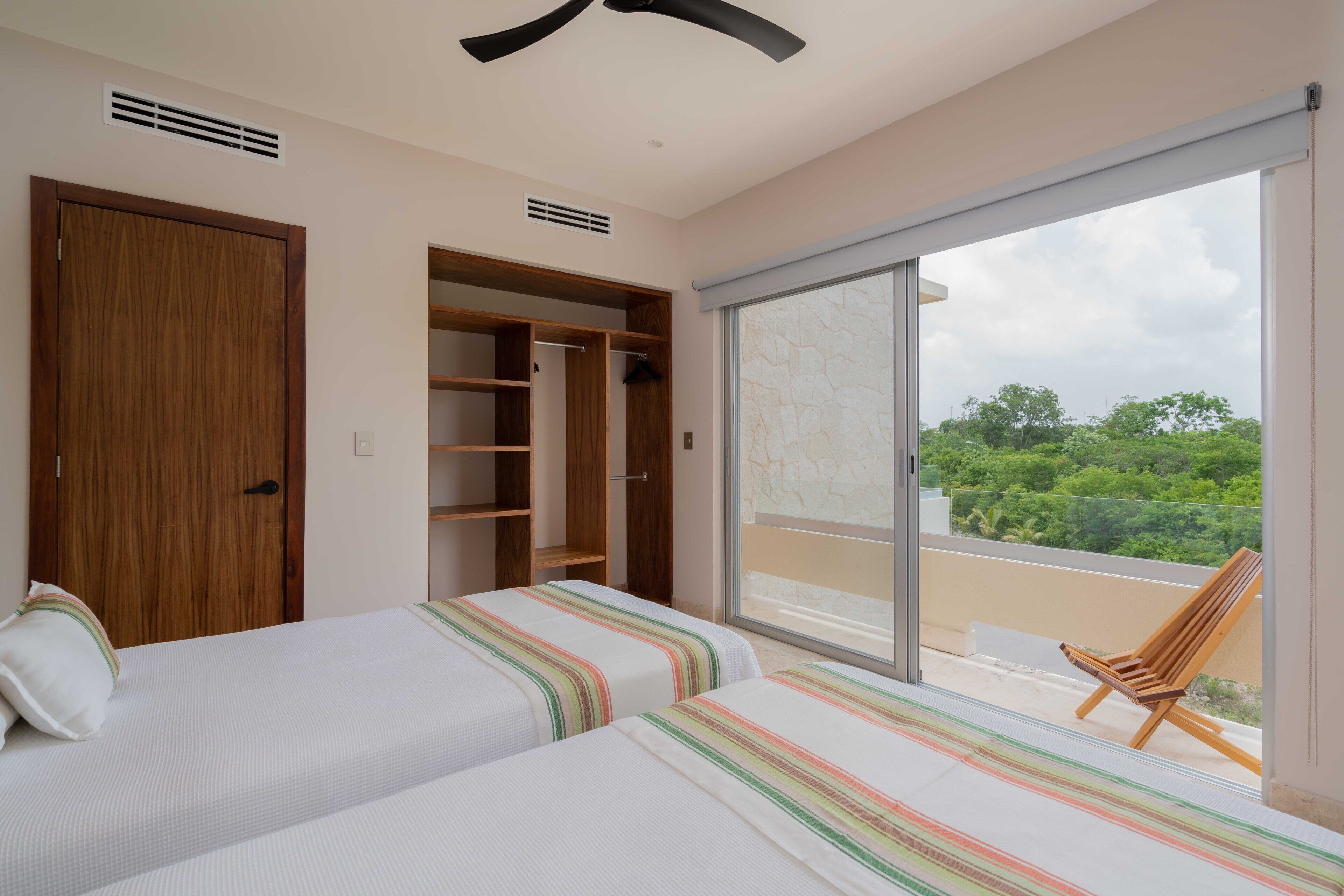 Un dormitorio con dos camas, un armario de madera y un ventanal corredera a un balcón.
