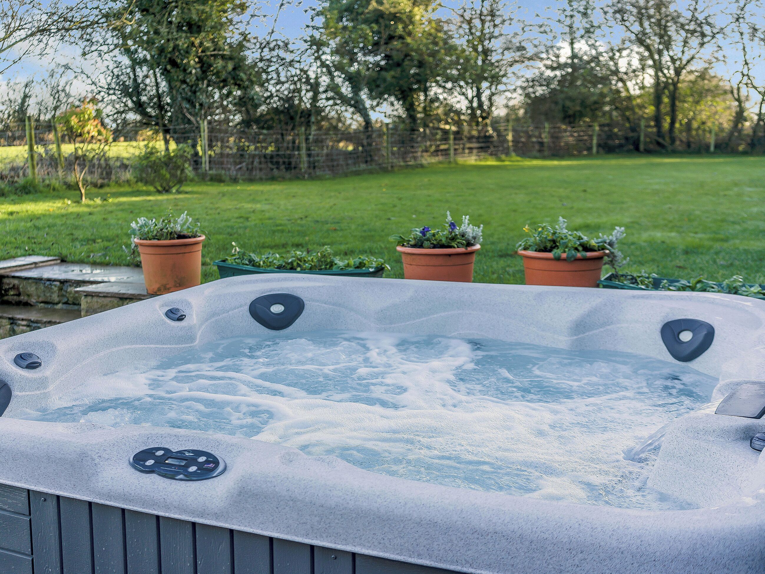 A hot tub in a garden with a grassy lawn and potted plants.